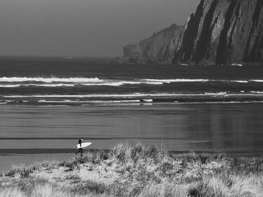 Someone carrying a surfboard with sea and cliffs in the background